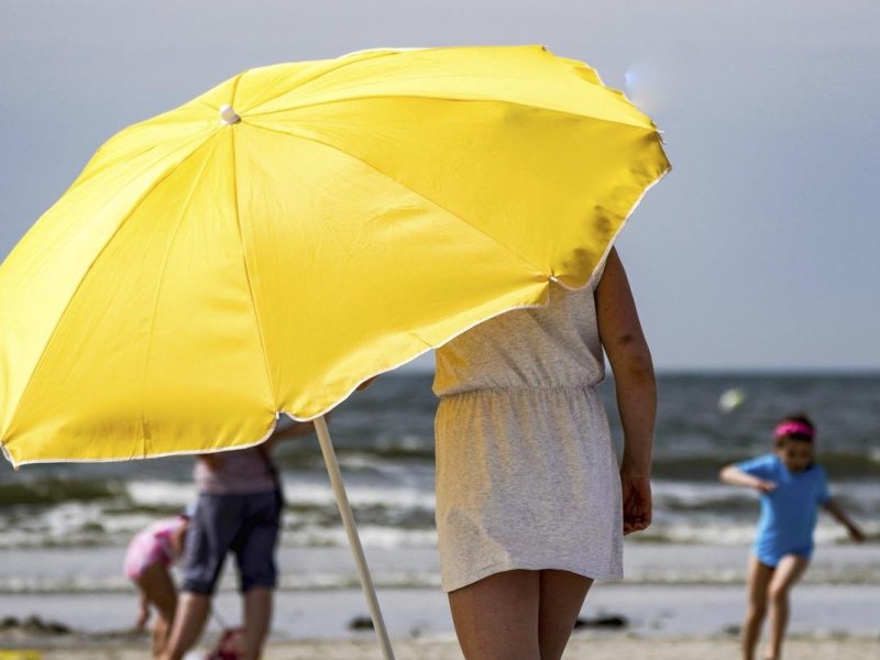 Eine Frau stellt in der gleißenden Sonne am Strand von St. Peter-Ording einen Sonnenschirm auf.