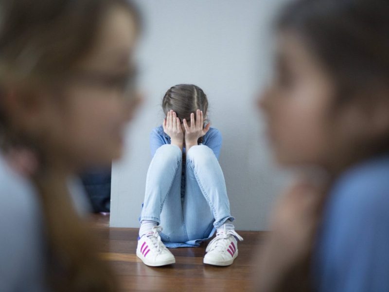 Mädchen mit Kopf in den Händen auf dem Boden sitzend