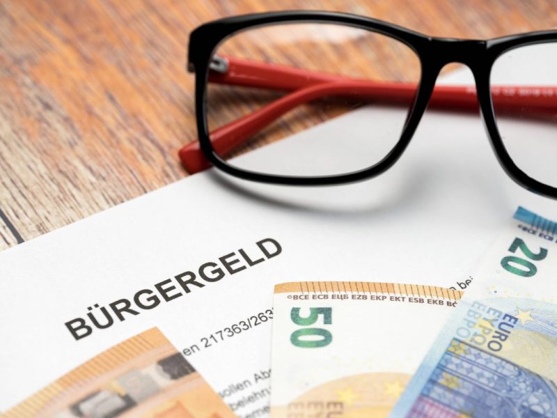 Eine Brille, ein Papier und Euroscheine liegen auf einem Tisch.