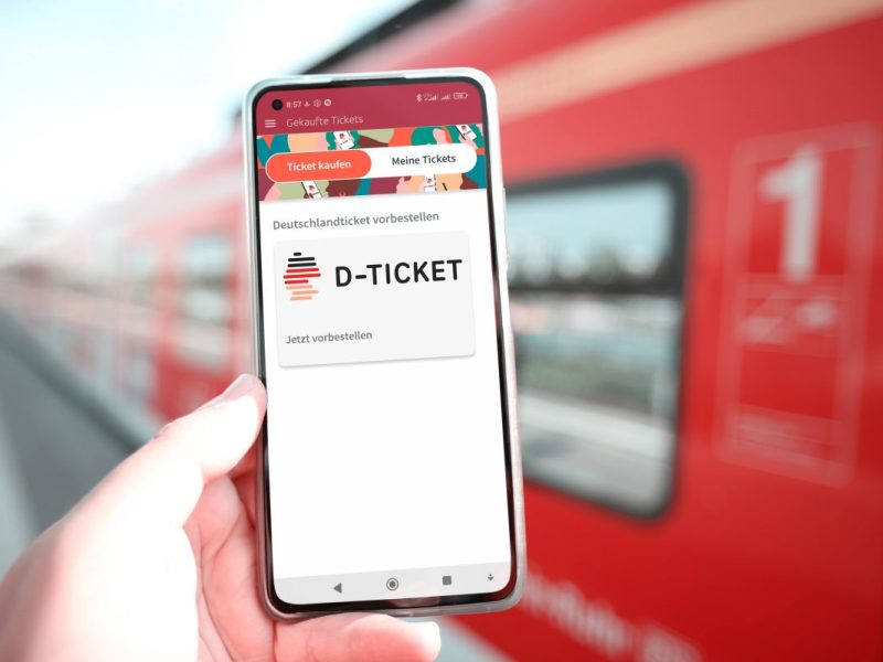 Deutschlandticket auf Handy mit Bahn im Hintergrund