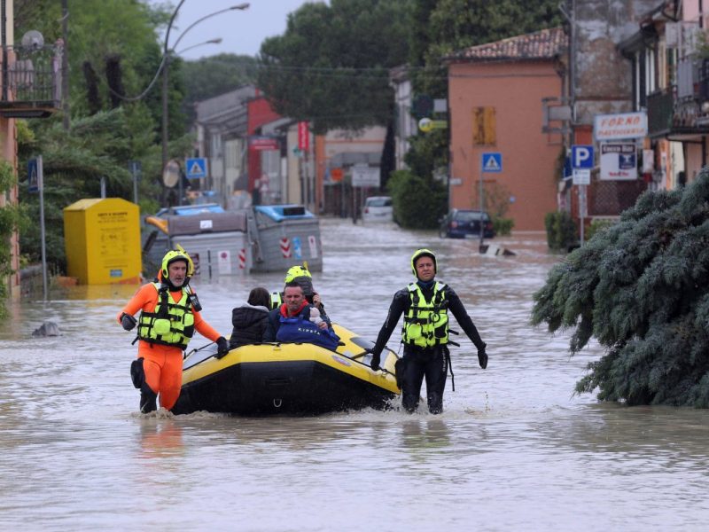 Rettungskräfte helfen Anwohnern in ein Schlauboot, während ihnen das Wasser bis zu den Knien steht.
