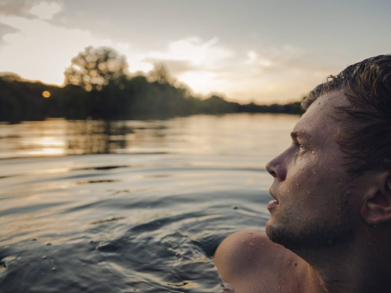 Junger Mann schwimmt im Wasser und schaut in den Himmel