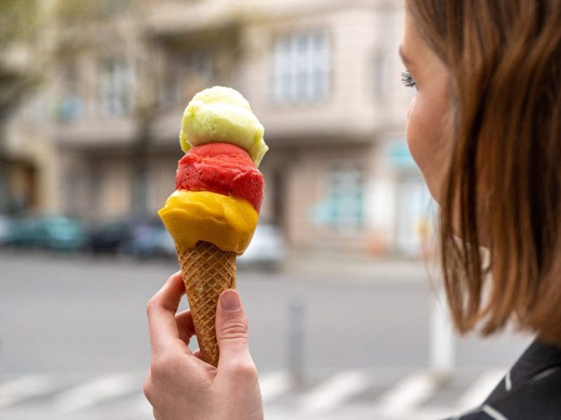 Frau hält Eistüte mit drei Fruchtkugeln in der Hand