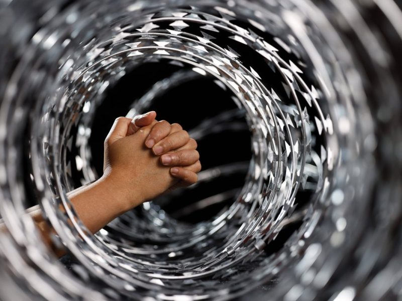 Frau faltet Hände im Stracheldrahtzaun