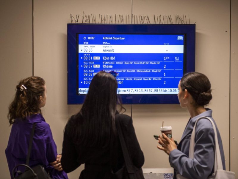 drei Frauen schauen sich die Fahrplanauskunft der Deutschen Bahn und Co. an