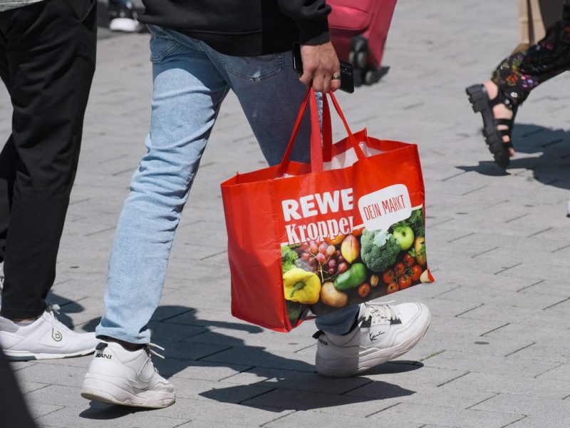 Frau trägt Rewe-Tragetasche