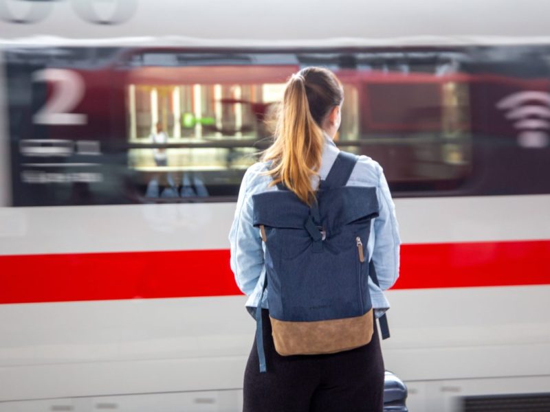 Frau seht vor einem vorbeifahrenden Zug der Deutschen Bahn
