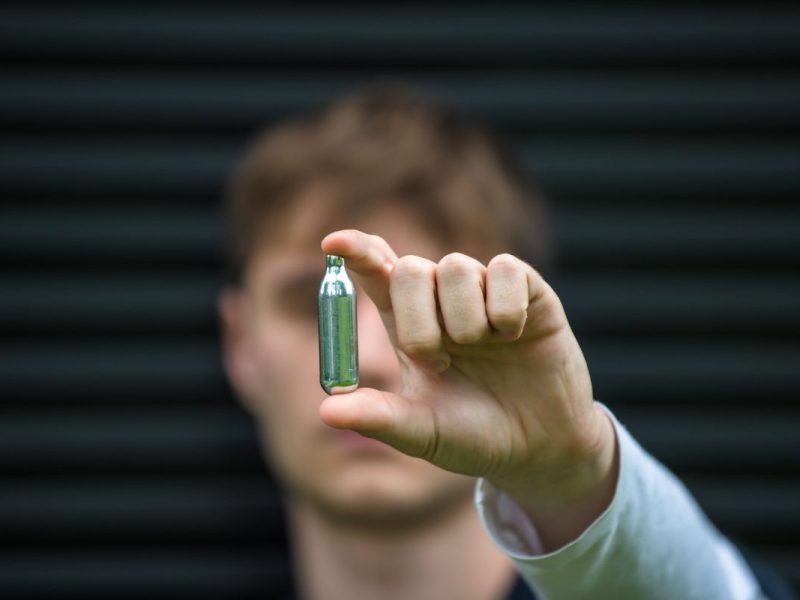 Junger Mann hält Lachgas-Kartusche in die Kamera
