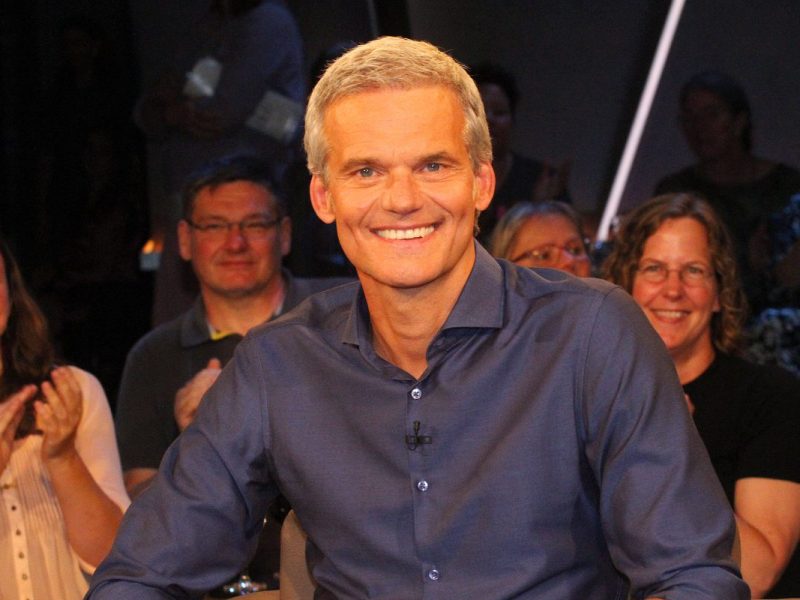 Auf dem Bild ist Tagesschau-Moderator Thorsten Schröder zu sehen. Er hat ein breites Grinsen aufgesetzt. Er hat graue hhochgegelte Haare und trägt ein blaues Hemd.