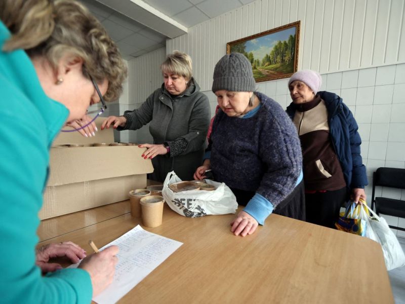 Drei ältere Damen stehen an einer Essensausgabe.