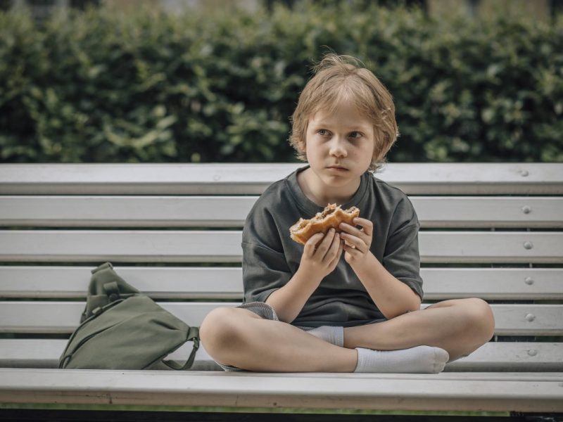 Kind isst Burger auf Bank